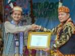 Bupati Mahulu, Dr. Bonifasius Belawan Geh menerima penghargaan atas terpilihnya Festival Hudoq Pekayang sebagai salah satu dari 110 event terbaik dalam Karisma Event Nusantara (KEN) 2024 yang diberikan langsung oleh perwakilan Kemenparekraf, Wilda. Foto: HO/Prokopim Mahulu