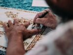 Ilustrasi. Seorang pembatik sedang menggambar sketas pola batik pada kain. Foto: Pexels