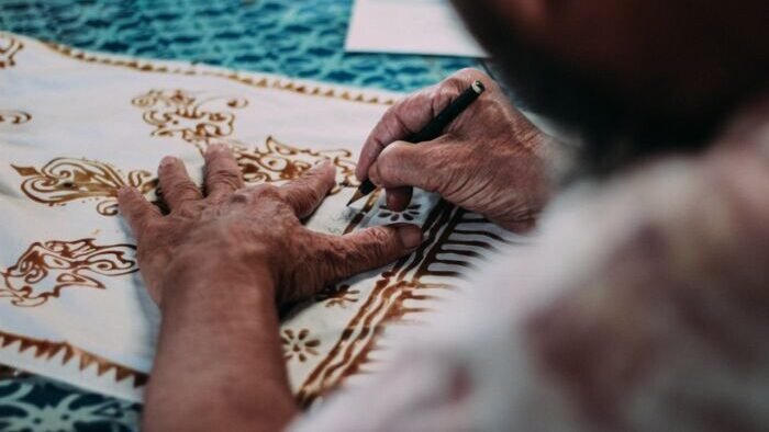 Ilustrasi. Seorang pembatik sedang menggambar sketas pola batik pada kain. Foto: Pexels